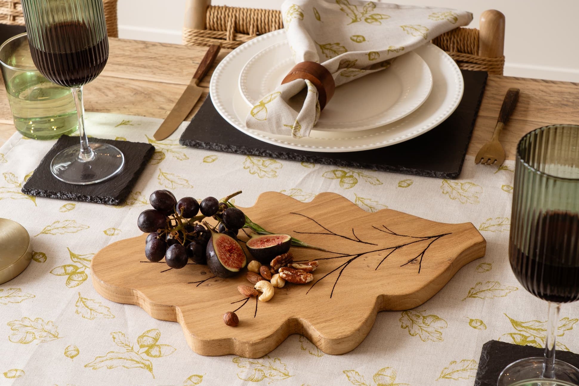 Dining table setting with plates, glasses, and a wooden cutting board with fruits.